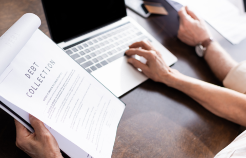 Person reviewing a debt collection notice while using a laptop at a desk