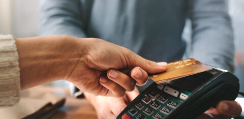 A person making a contactless payment with a credit card at a point-of-sale terminal.