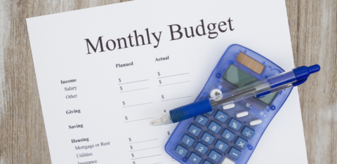 Monthly budget worksheet with a pen and calculator on a wooden table.