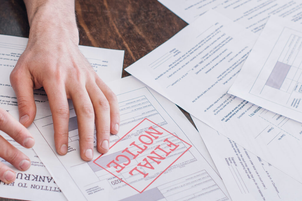 A person's hand resting on a stack of financial documents, with one paper prominently stamped “FINAL NOTICE” in red.