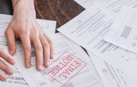 A person's hand resting on a stack of financial documents, with one paper prominently stamped “FINAL NOTICE” in red.
