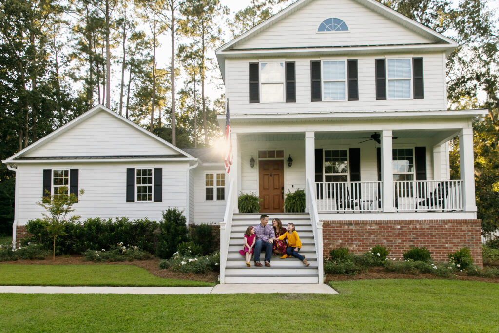 Family sitting on the front steps of a white suburban home with black shutters, enjoying time together outdoors.