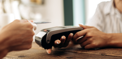 Close-up of a credit card being tapped on a card reader, with a cashier holding the payment terminal.