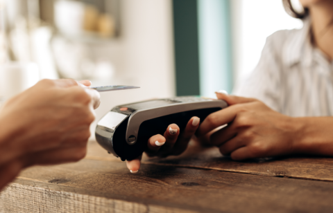Close-up of a credit card being tapped on a card reader, with a cashier holding the payment terminal.