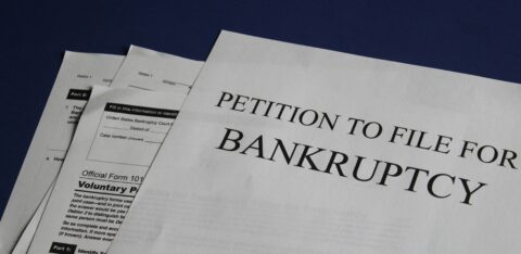Close-up of bankruptcy petition paperwork on a dark surface, showing official forms for filing Chapter 7 or Chapter 13.