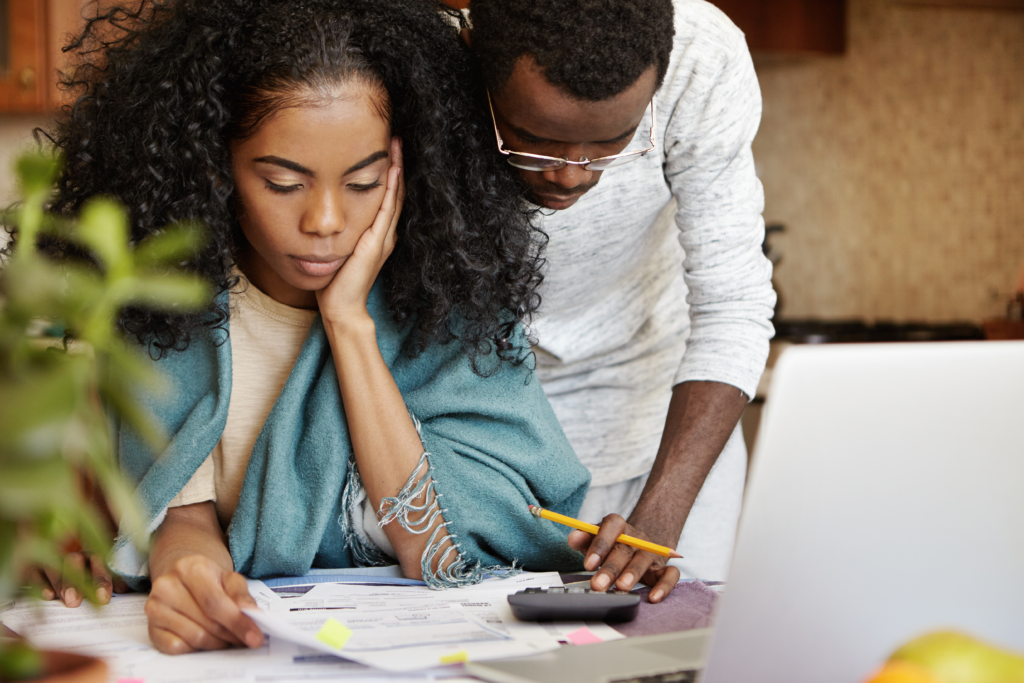 Couple reviewing financial documents together at home, looking concerned.