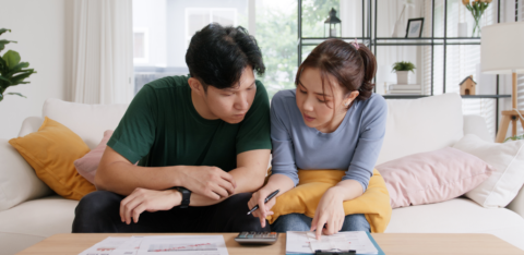 Young couple sitting on a couch, focused on calculating finances with bills and documents spread out on the table.