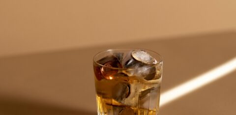 Glass of whiskey on a tan surface with coins and ice cubes inside