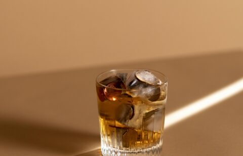 Glass of whiskey on a tan surface with coins and ice cubes inside