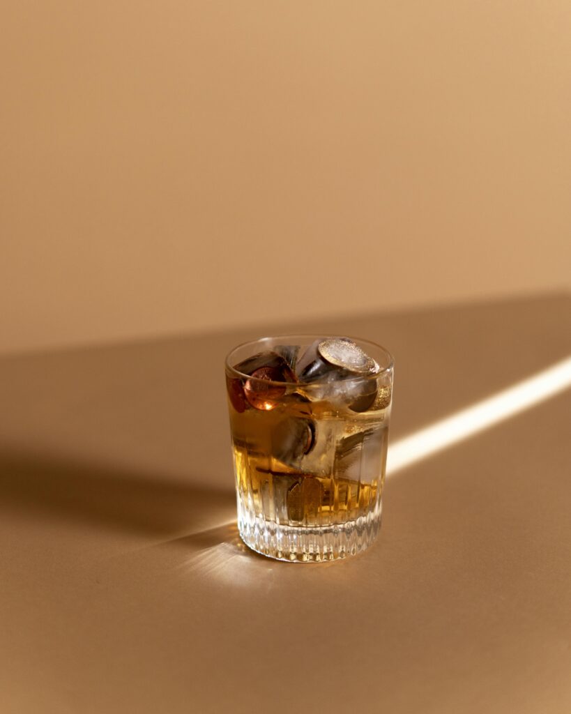 Glass of whiskey on a tan surface with coins and ice cubes inside