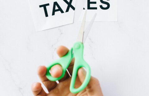 Close-up of a person cutting a “TAXES” sign with scissors