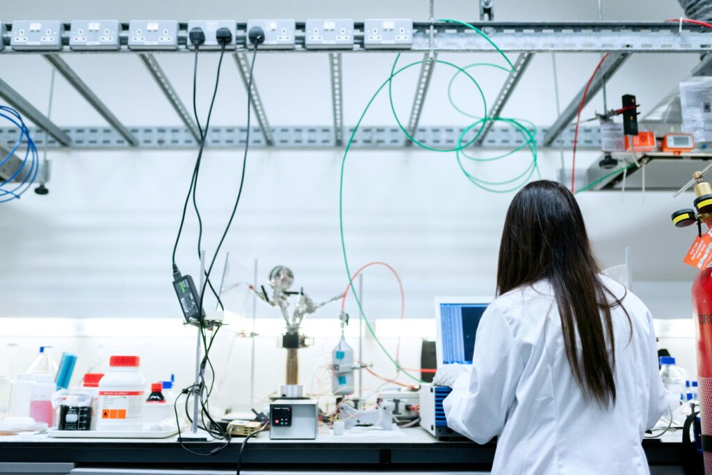 Researcher in a white lab coat analyzing data on a computer in a modern lab filled with wires, tubes, and lab tools.