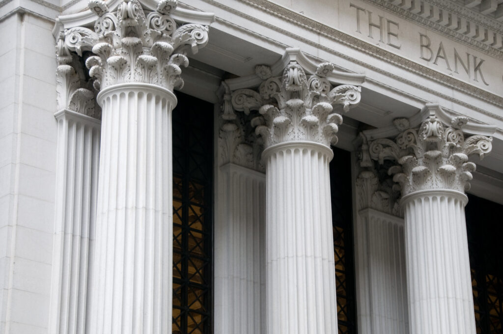 Close-up of Corinthian columns on the facade of a traditional stone bank building with 'THE BANK' engraved above.