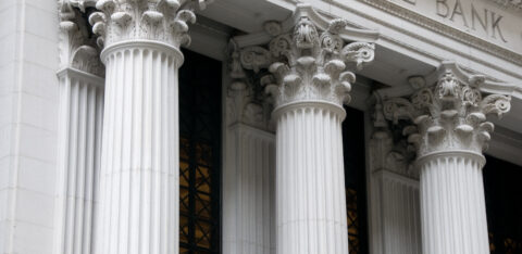 Close-up of Corinthian columns on the facade of a traditional stone bank building with 'THE BANK' engraved above.