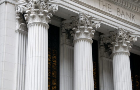 Close-up of Corinthian columns on the facade of a traditional stone bank building with 'THE BANK' engraved above.