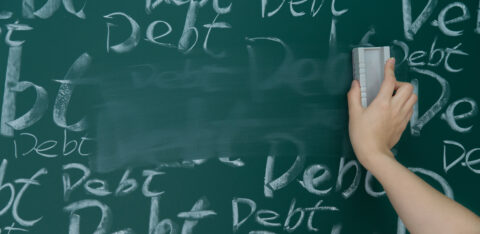 Hand erasing the word “debt” repeatedly written on a chalkboard