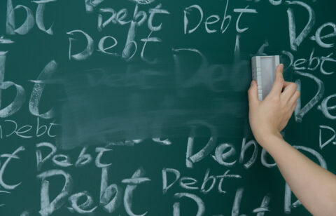 Hand erasing the word βdebtβ repeatedly written on a chalkboard