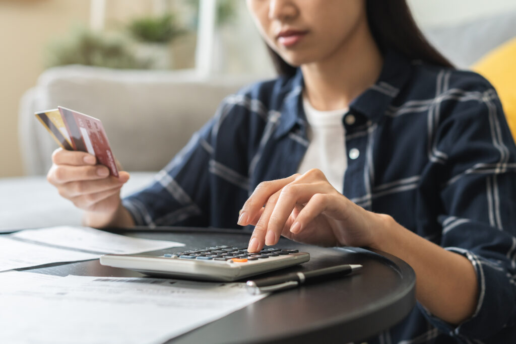 Woman calculating expenses with a credit card in hand, surrounded by bills and financial documents.