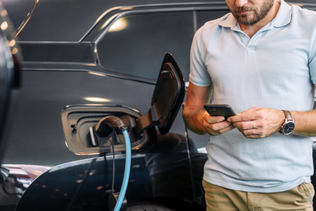 Man using a smartphone while charging an electric vehicle.
