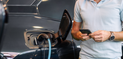 Man using a smartphone while charging an electric vehicle.