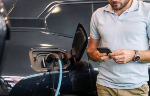 Man using a smartphone while charging an electric vehicle.