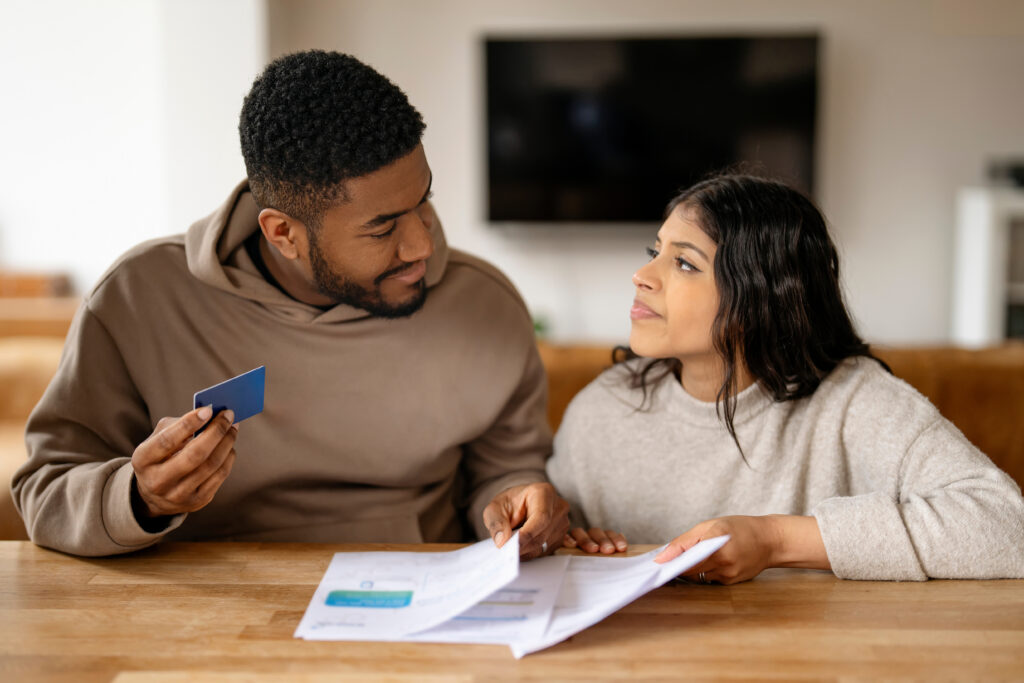 Young couple reviewing bills together at a table, holding a credit card