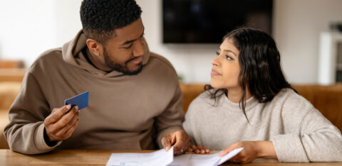 Young couple reviewing bills together at a table, holding a credit card
