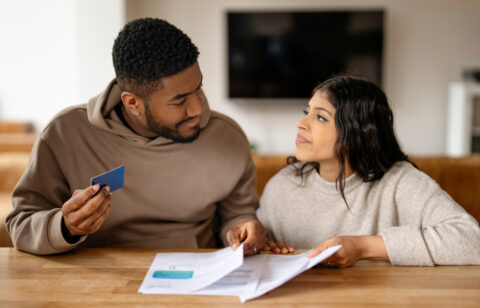 Young couple reviewing bills together at a table, holding a credit card