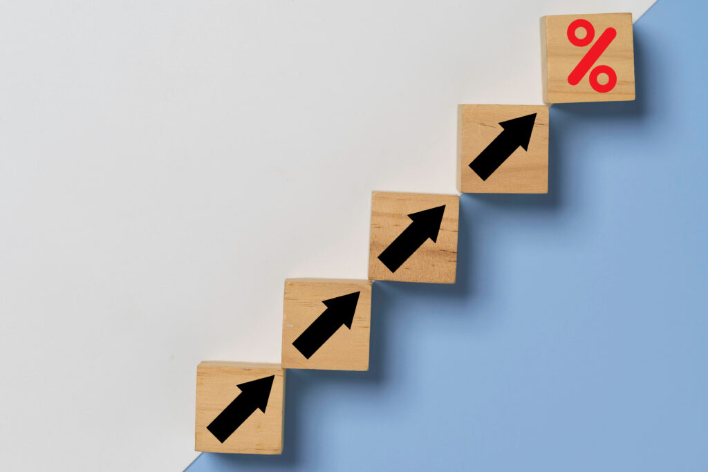 Conceptual staircase made of wooden cubes showing increasing arrows, ending in a percentage sign to represent growing interest rates or debt.