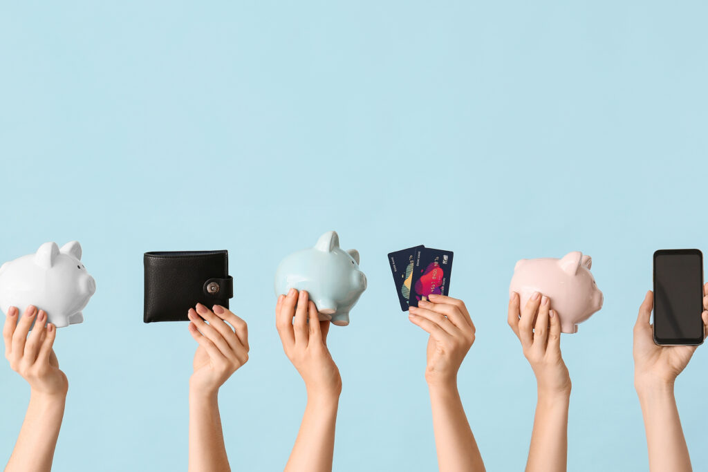 Hands holding piggy banks, a wallet, credit cards, and a smartphone against a blue background