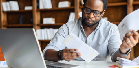 Person reviewing financial documents at a desk with a laptop and papers.
