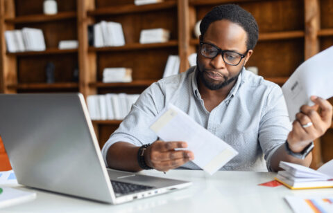 Person reviewing financial documents at a desk with a laptop and papers.