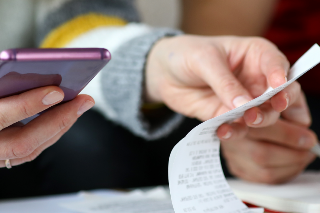 Close-up of two people reviewing a receipt and using a smartphone, suggesting budgeting or expense tracking.