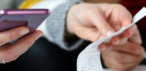 Close-up of two people reviewing a receipt and using a smartphone, suggesting budgeting or expense tracking.