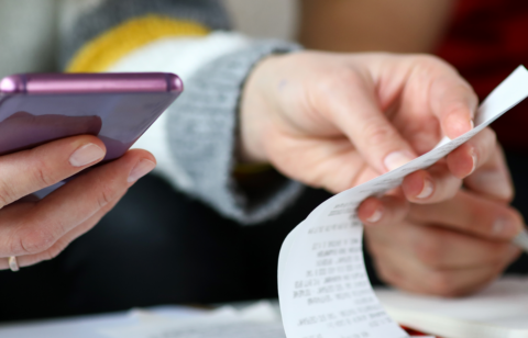 Close-up of two people reviewing a receipt and using a smartphone, suggesting budgeting or expense tracking.
