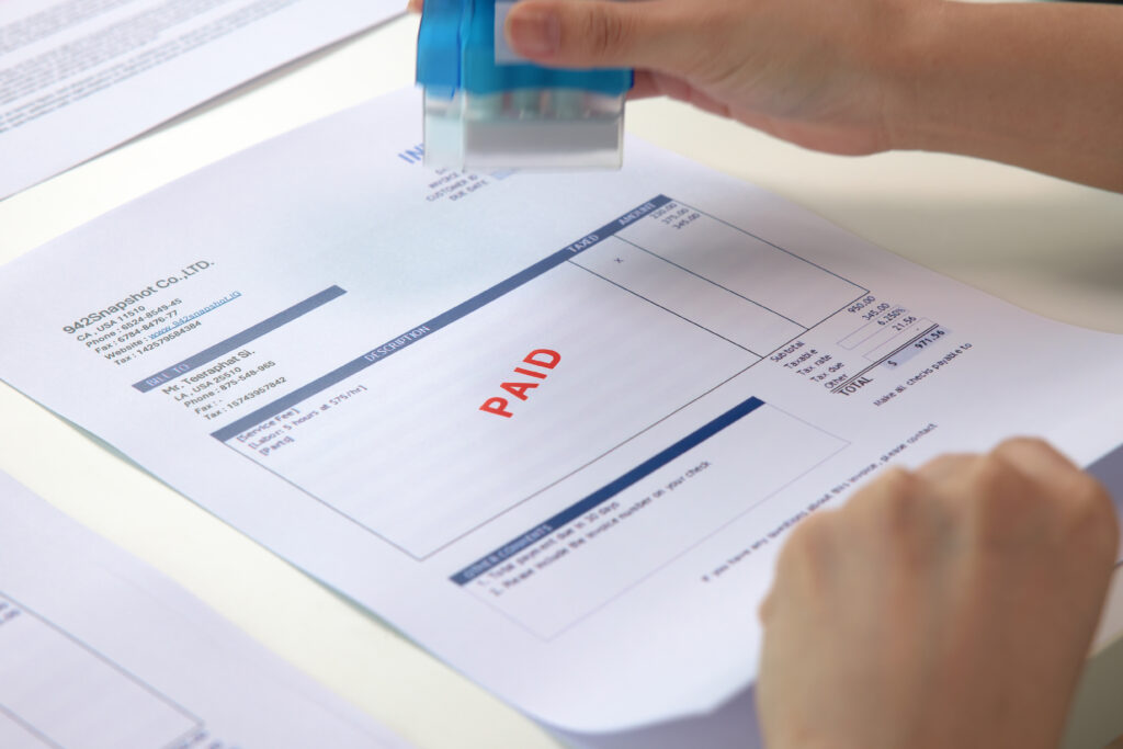 Close-up of a person stamping an invoice with the word 'PAID' in red, showing a completed payment on a financial document.