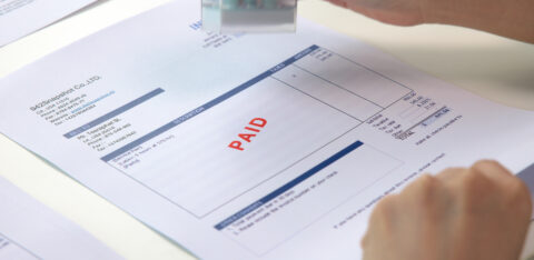 Close-up of a person stamping an invoice with the word 'PAID' in red, showing a completed payment on a financial document.