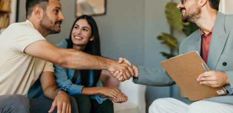 Smiling couple meeting with a professional holding a clipboard, as the man and the advisor shake hands in a friendly office setting.