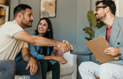 Smiling couple meeting with a professional holding a clipboard, as the man and the advisor shake hands in a friendly office setting.