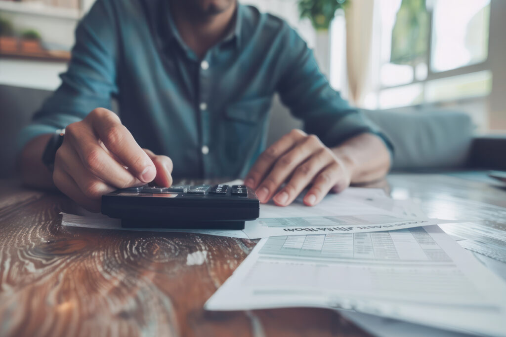 Person using a calculator while reviewing bills and financial documents at home