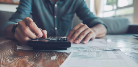 Person using a calculator while reviewing bills and financial documents at home