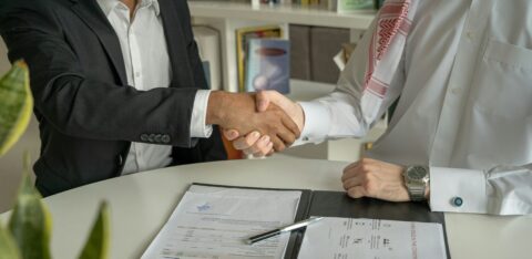 Two men shaking hands over a signed agreement at a desk
