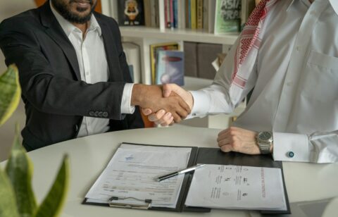 Two men shaking hands over a signed agreement at a desk