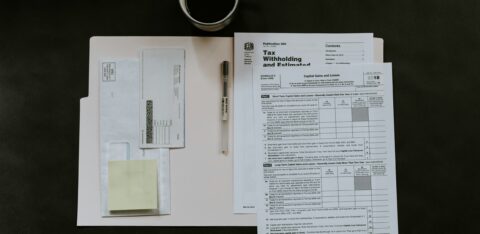Tax forms and a pen organized on a folder, with a cup of coffee nearby.