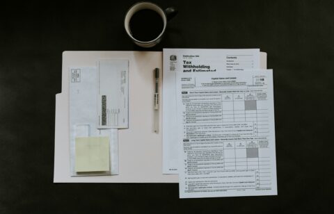 Tax forms and a pen organized on a folder, with a cup of coffee nearby.