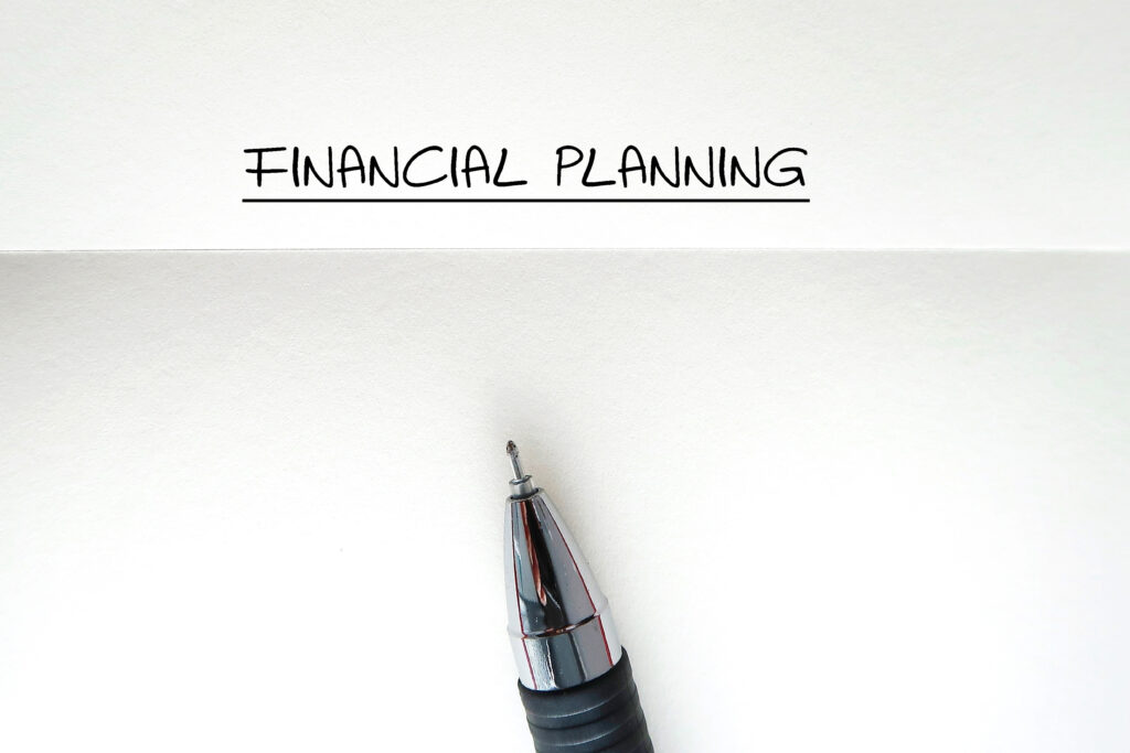 Close-up of a pen below the handwritten words 'Financial Planning' underlined on a blank sheet of paper.