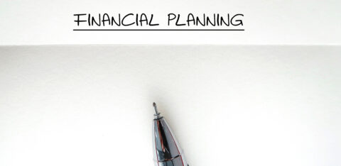 Close-up of a pen below the handwritten words 'Financial Planning' underlined on a blank sheet of paper.