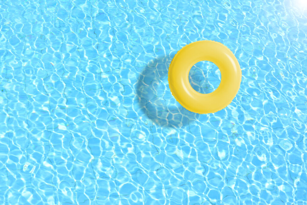 Yellow inflatable swim ring floating in a clear blue swimming pool on a sunny day.