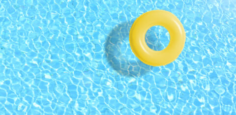 Yellow inflatable swim ring floating in a clear blue swimming pool on a sunny day.