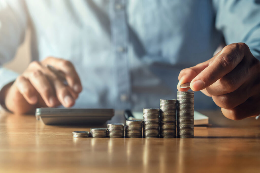 Person stacking coins in increasing height next to a calculator on a desk